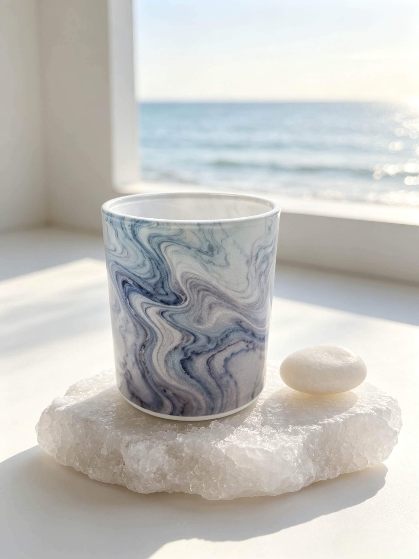 Empty blue marble glass candle vessel resting on a white sea salt stone against an ocean background for aquatic scent lines