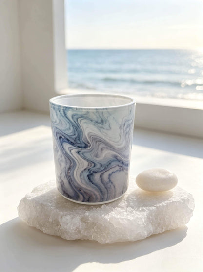 Empty blue marble glass candle vessel resting on a white sea salt stone against an ocean background for aquatic scent lines