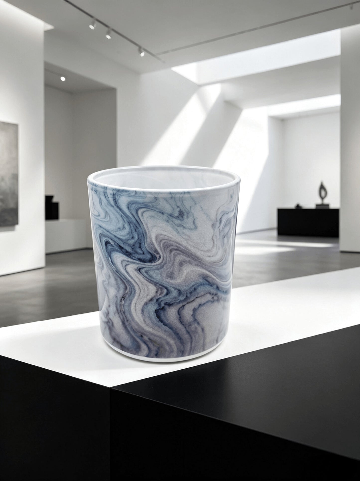 Empty blue marble fluid ink candle jar styled on a black and white pedestal in a modern art gallery setting