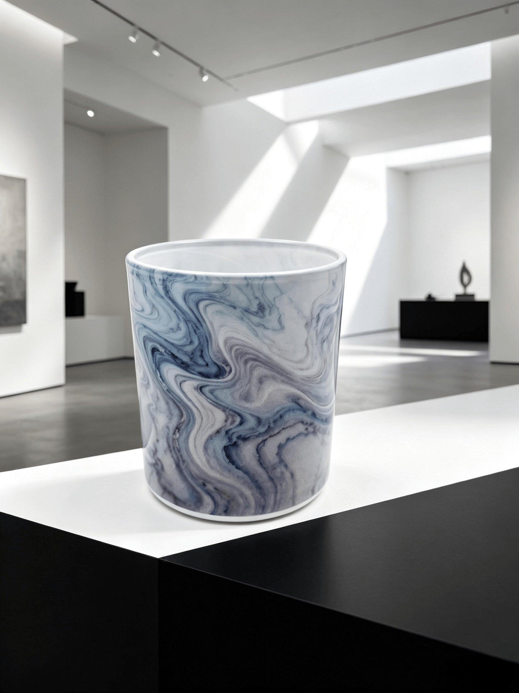 Empty blue marble fluid ink candle jar styled on a black and white pedestal in a modern art gallery setting