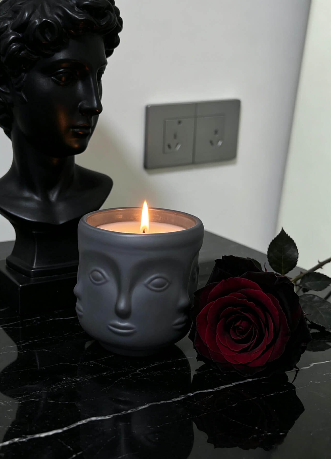 Lit matte black 3D face candle glass styled with a dark red rose and classical bust for dark romantic fragrance lines