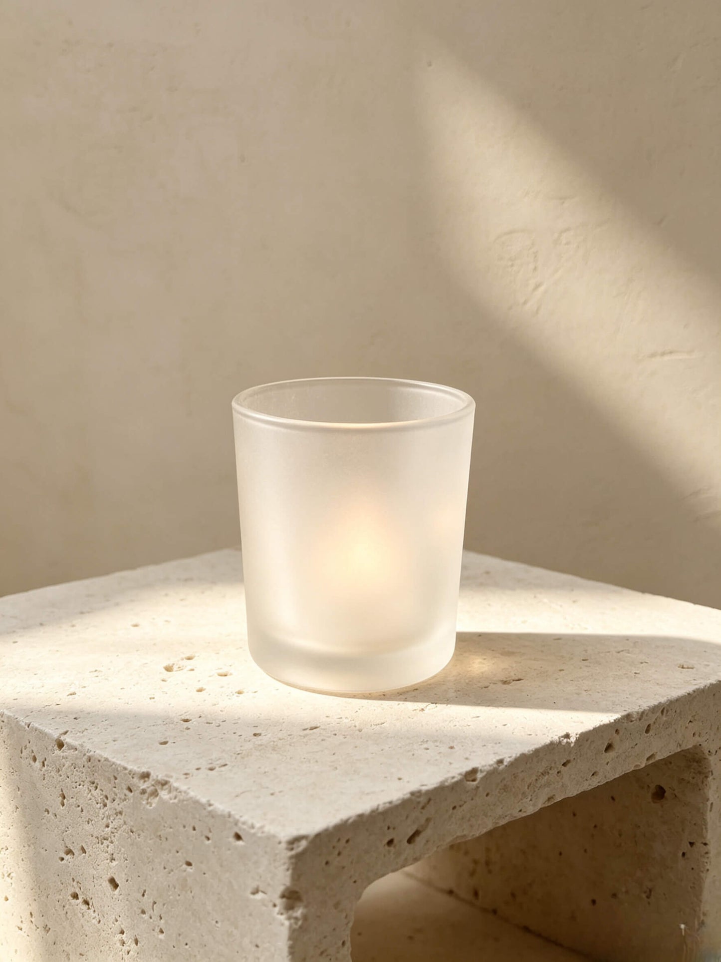 Lit frosted white candle jar on a travertine stone block showing Japandi and wabi sabi aesthetic