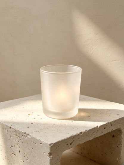 Lit frosted white candle jar on a travertine stone block showing Japandi and wabi sabi aesthetic