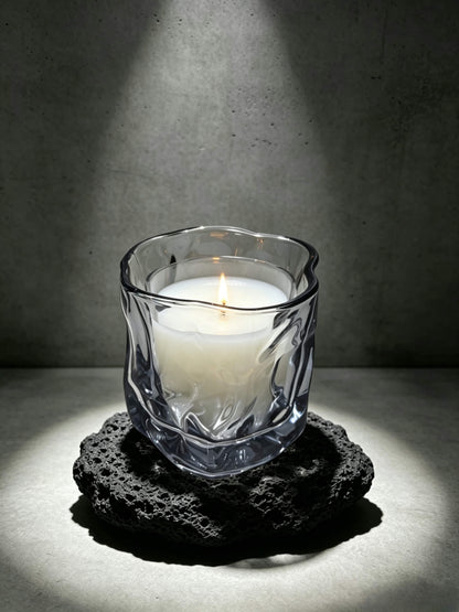 Lit smoky quartz wabi sabi folded candle vessel resting on a dark brutalist lava stone