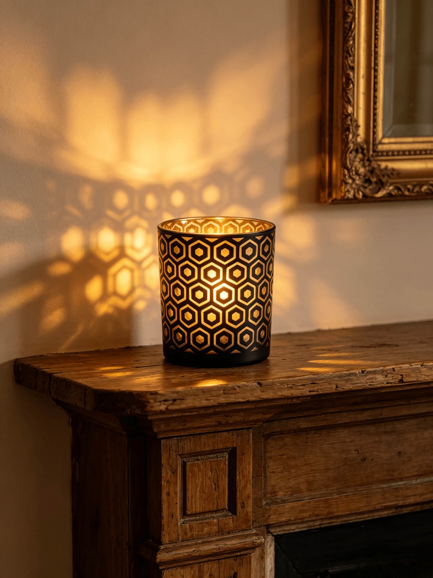 Lit hexagon cut out glass candle vessel glowing with gold light projections on a rustic wood mantel