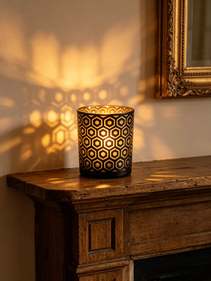 Lit hexagon cut out glass candle vessel glowing with gold light projections on a rustic wood mantel