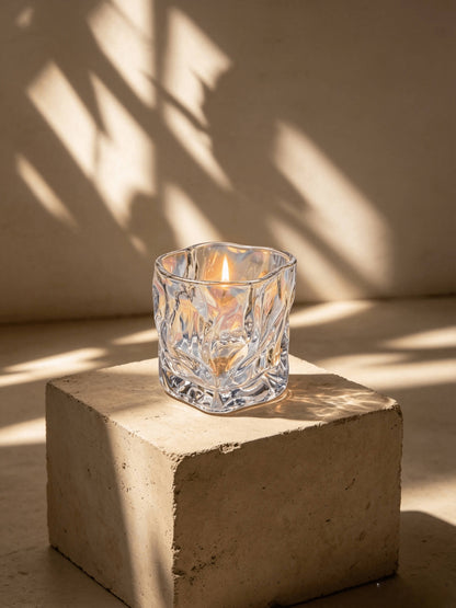 Lit iridescent wabi sabi folded candle vessel glowing in natural sunlight on a minimalist stone block
