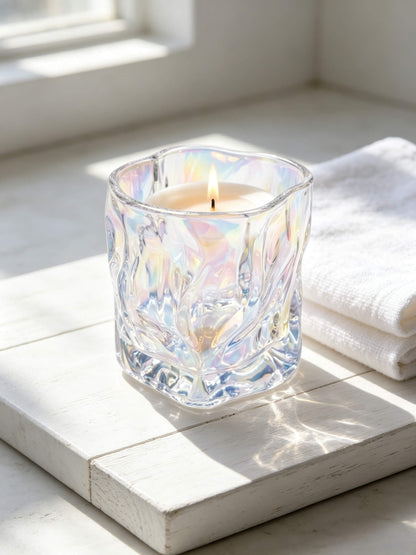 Lit iridescent glass candle jar next to a white towel for luxury clean beauty and wellness spa aesthetics