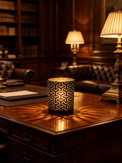 Lit matte black and gold labyrinth cut out candle jar casting dynamic light projections on a dark wood executive desk
