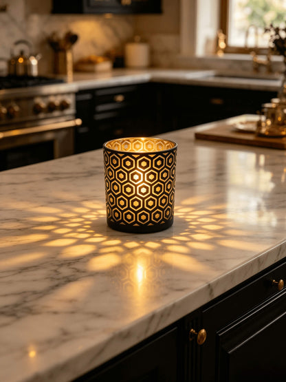 Lit matte black and gold hexagon cut out candle jar casting geometric light projection on a luxury marble kitchen island