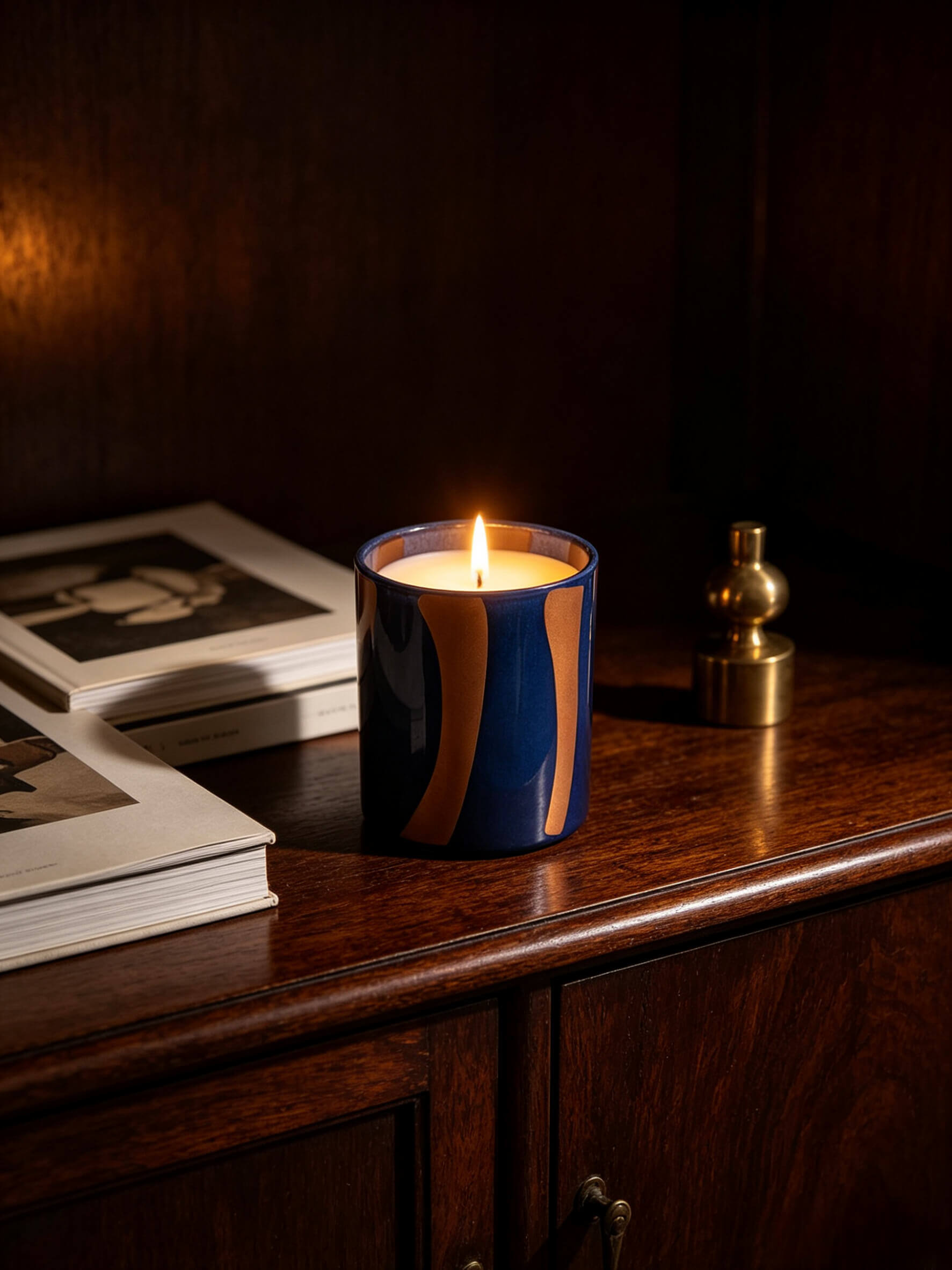 Lit military blue and ochre striped candle glass on dark wood credenza showing moody mid century modern aesthetic