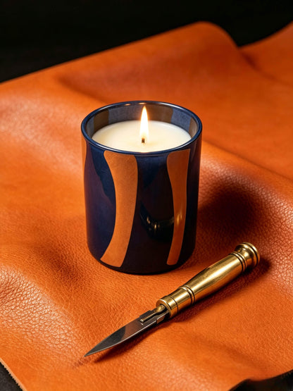 Lit modern color block glass candle vessel on orange pebbled leather for rich woody and leather scent profiles