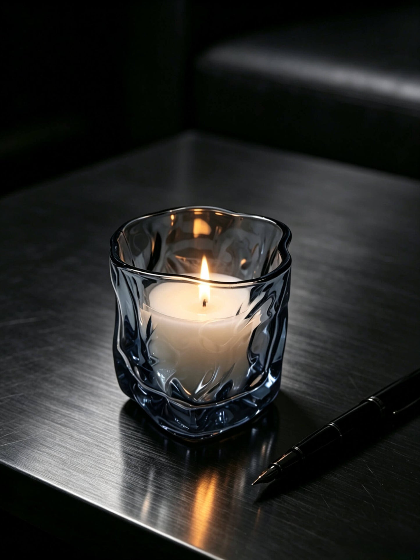 Lit smoky quartz artisan glass candle vessel styled on a dark gentleman desk for masculine fragrance lines