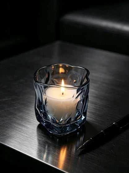 Lit smoky quartz artisan glass candle vessel styled on a dark gentleman desk for masculine fragrance lines