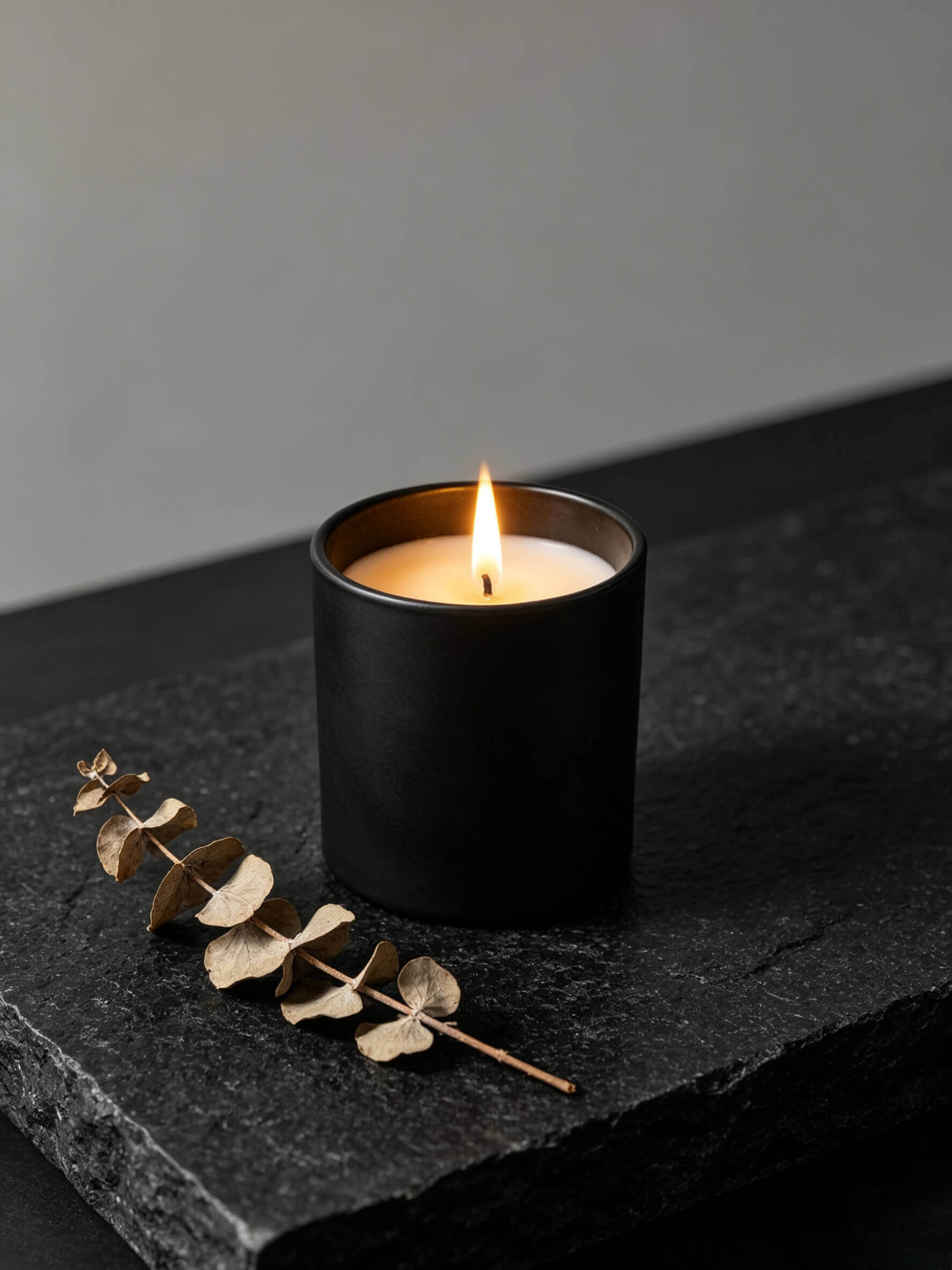Lit matte black candle vessel styled with dark stones and dry branch for moody holistic wellness decor