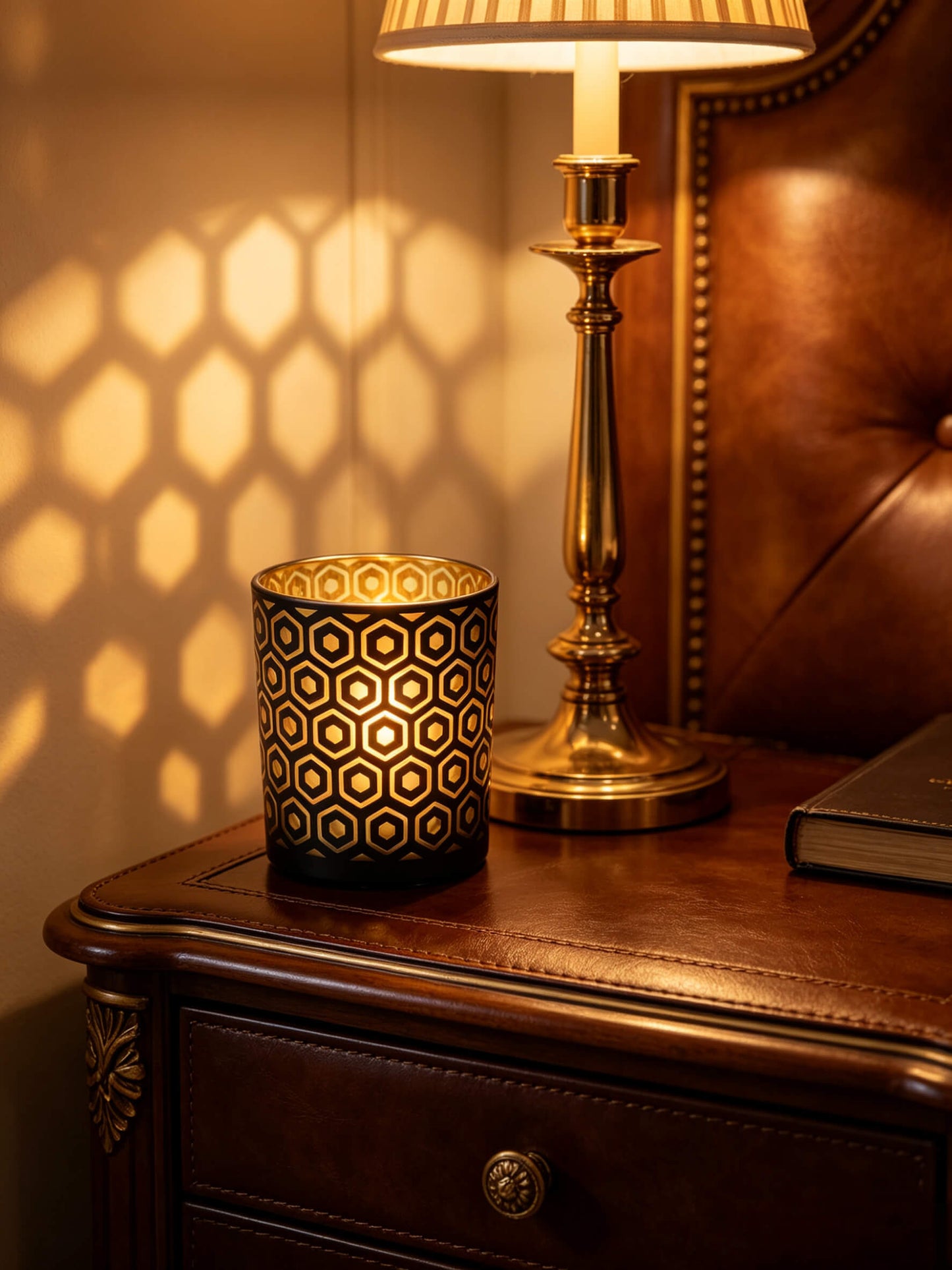 Lit black and gold hexagon candle jar casting architectural light shadows on a dark wood nightstand for old money aesthetic
