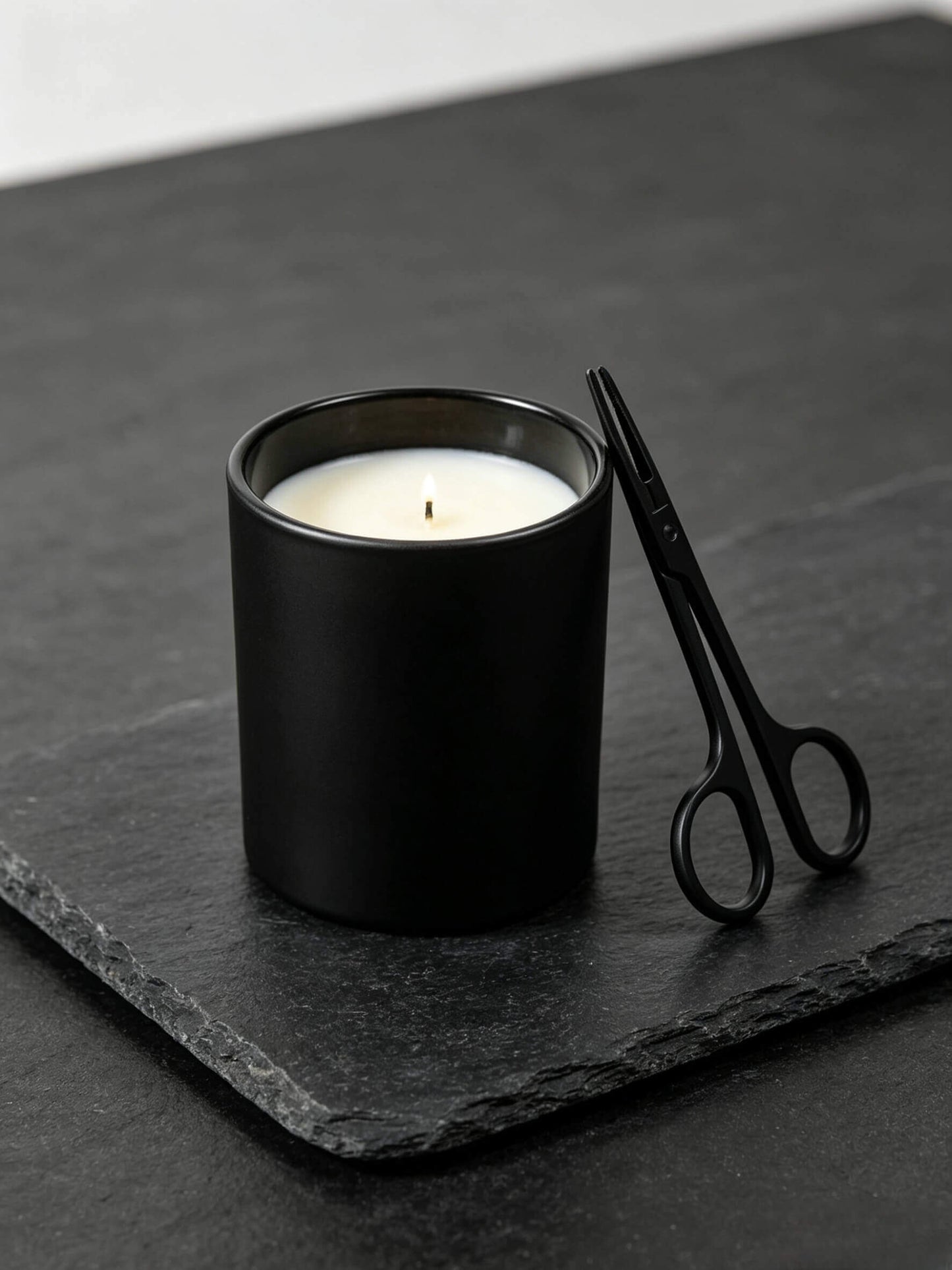 Empty matte black candle jar styled on dark slate with black wick trimmer for minimalist home fragrance lines